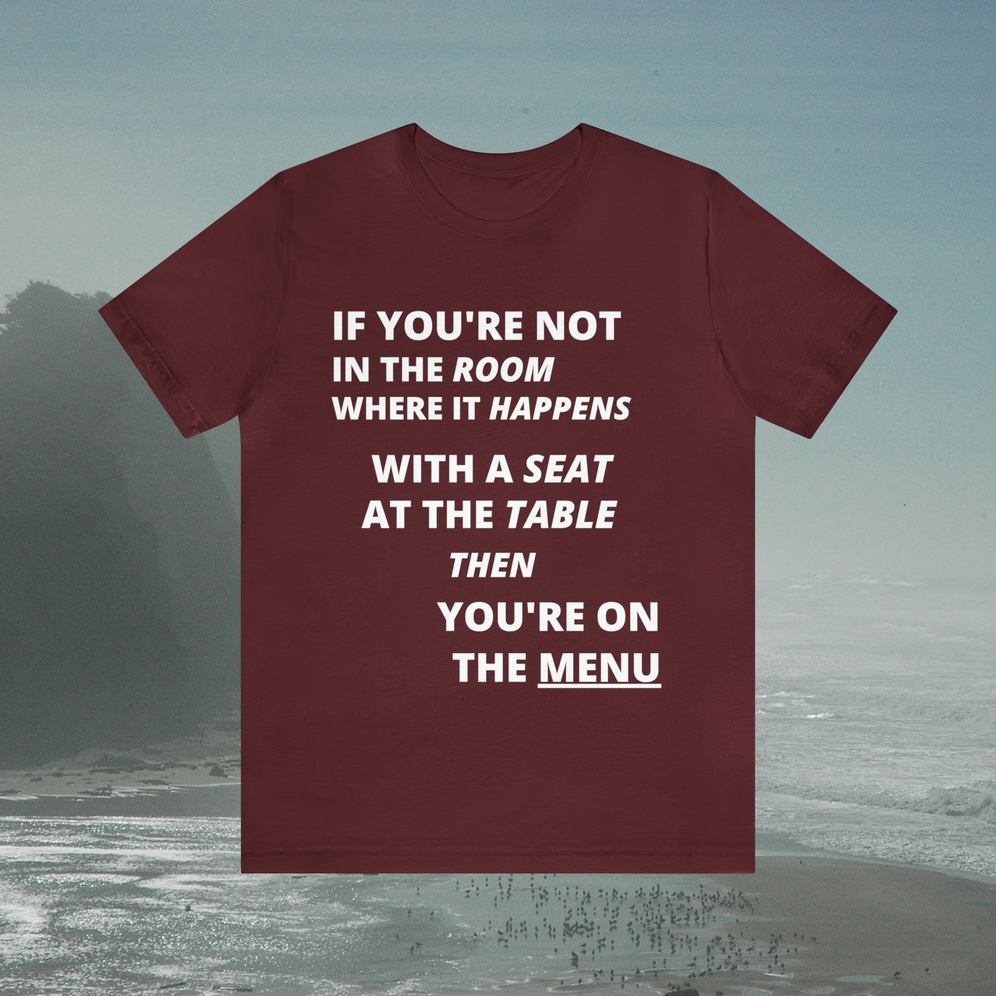 Maroon tee with graphic "If you're not in the room...", foggy seashore background.