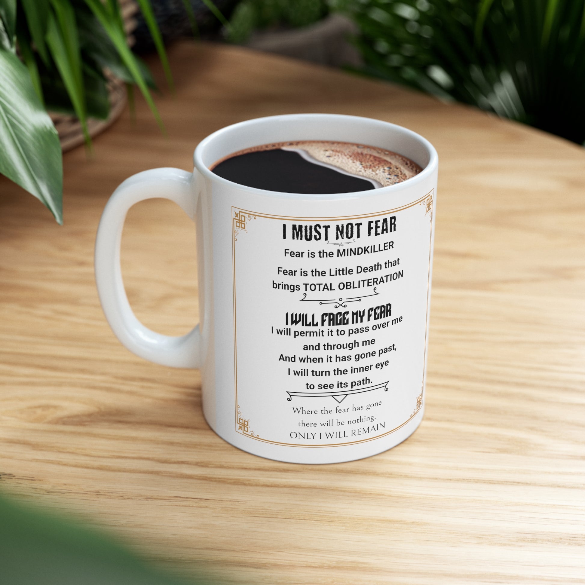 White mug with Dune's "Fear Litany" set on a wood table near a plant