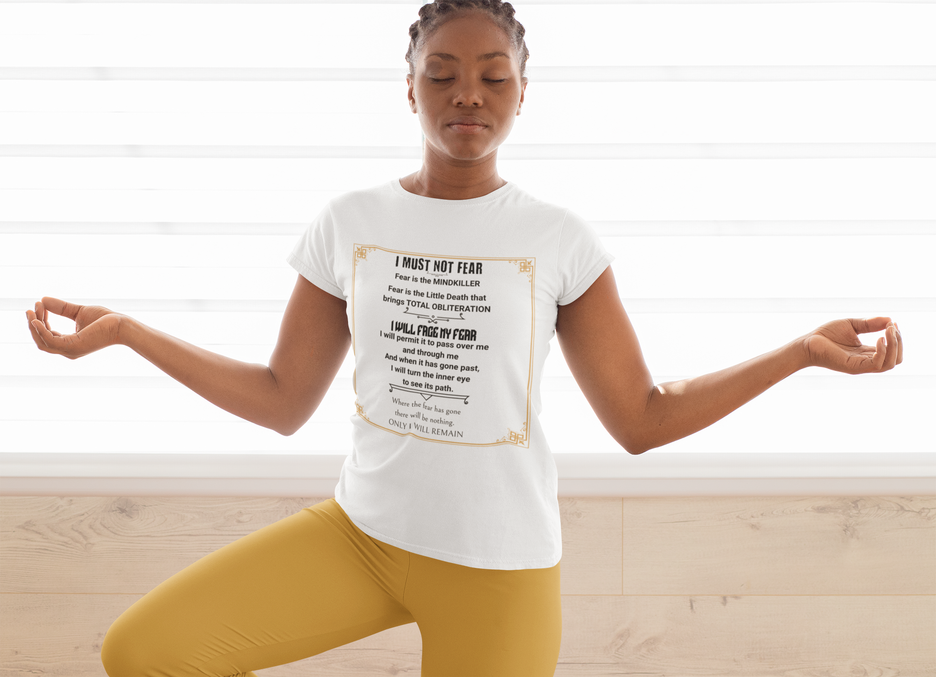 Young woman doing tree pose wearing a white tee with graphic"Fear Litany"