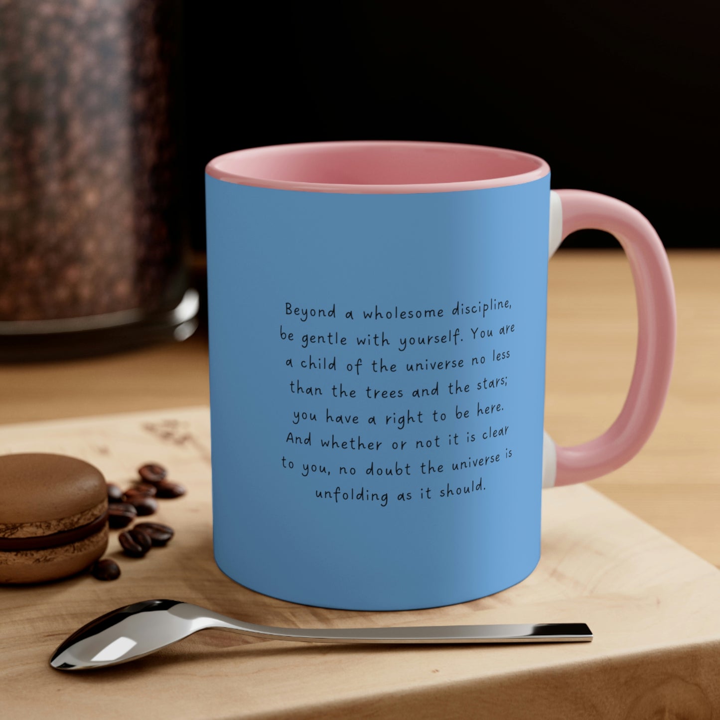 Blue mug with pink interior and handle, with quote "Desiderata, You are a Child of the Universe"  sitting on a wood block by a spoon.