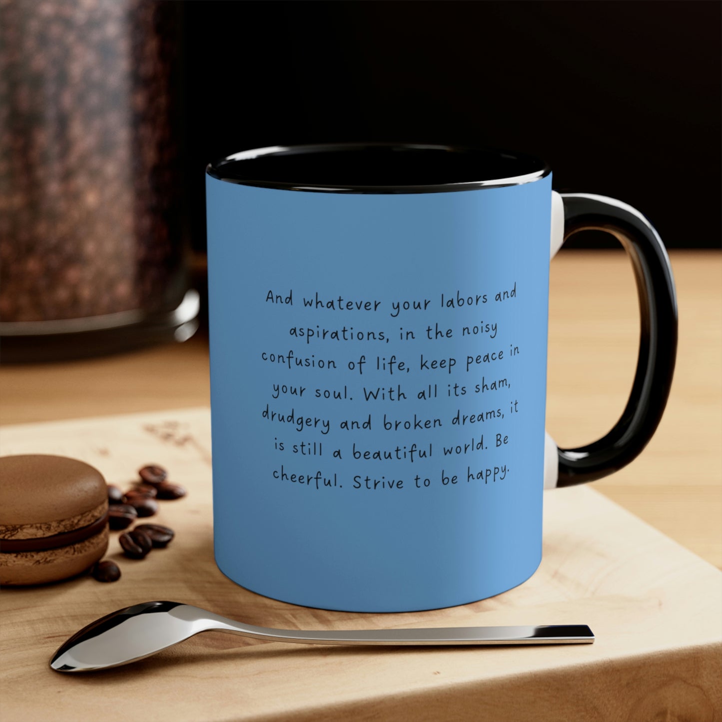 Black handle andi nsides  "Desiderata, Strive to   be Happy" blue mug on wood table by a spoon